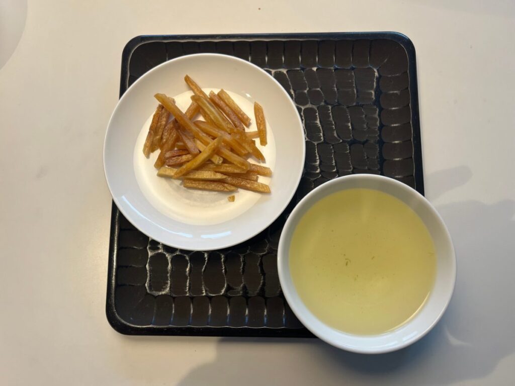 黒い角盆の上に、白い皿に盛った芋屋金次郎の黒糖芋けんぴと、土佐の緑茶を注いだ白い湯呑を並べたところ